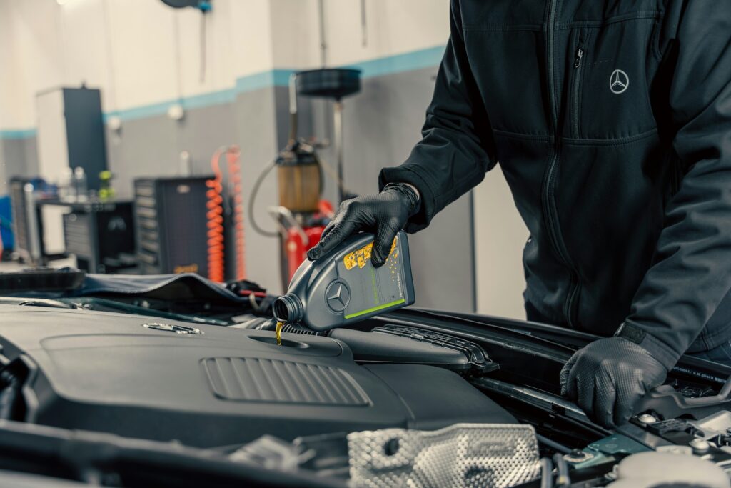 Mechanic in gloves topping up engine oil during a car service